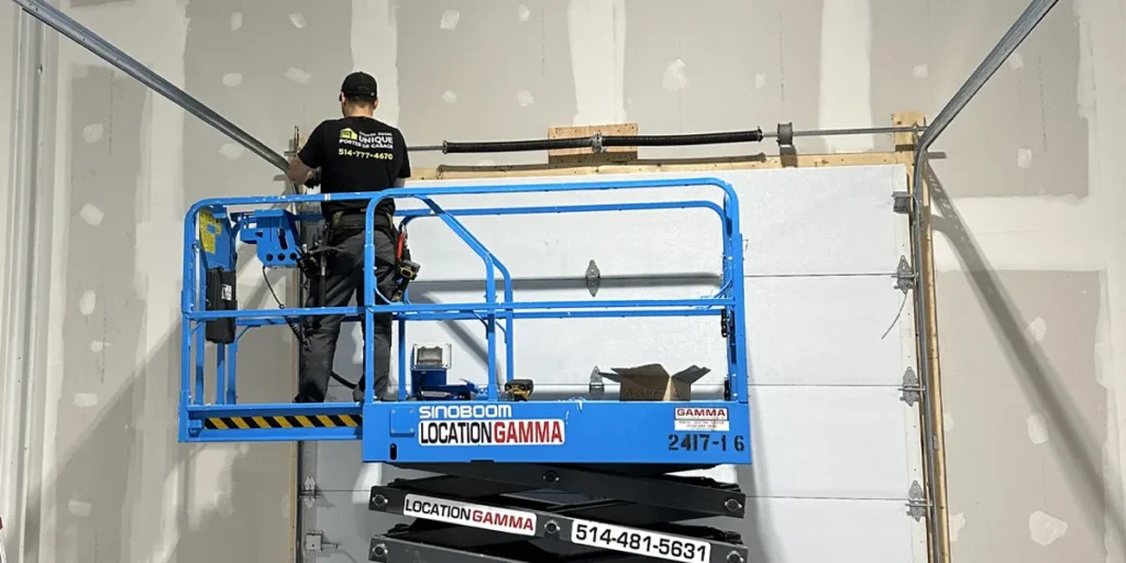 un spécialiste en réparation et maintenance de portes de garage utilisant un équipement avancé comme une nacelle à ciseaux pour installer une nouvelle porte de garage à Brossard